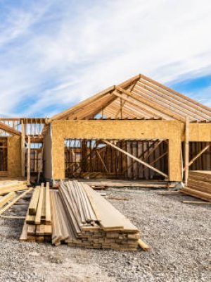 New house under construction, front view from garage door entry with clouds blue sky. Framing of home exterior structure with a pile of lumber and siding plank leftover. Real estate business industry.